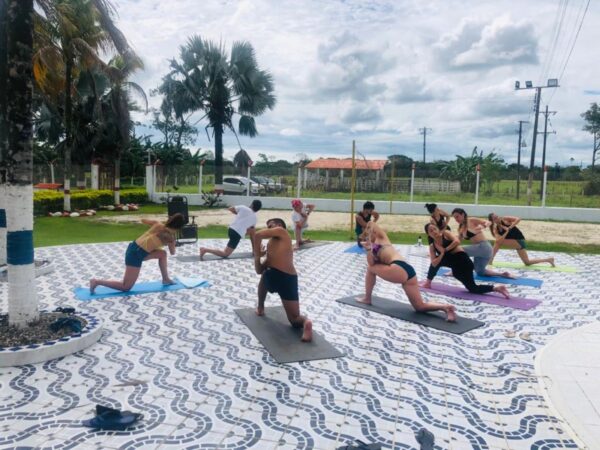 Clase Grupal presencial (mas de 3 personas) Sesión de yoga al aire libre con un grupo en postura de Guerrero, brazos extendidos y piernas dobladas en esterillas coloridas